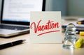 Ã¢â¬ÅVacationÃ¢â¬Â note on office desk. Laptop supplies, blurred background Royalty Free Stock Photo